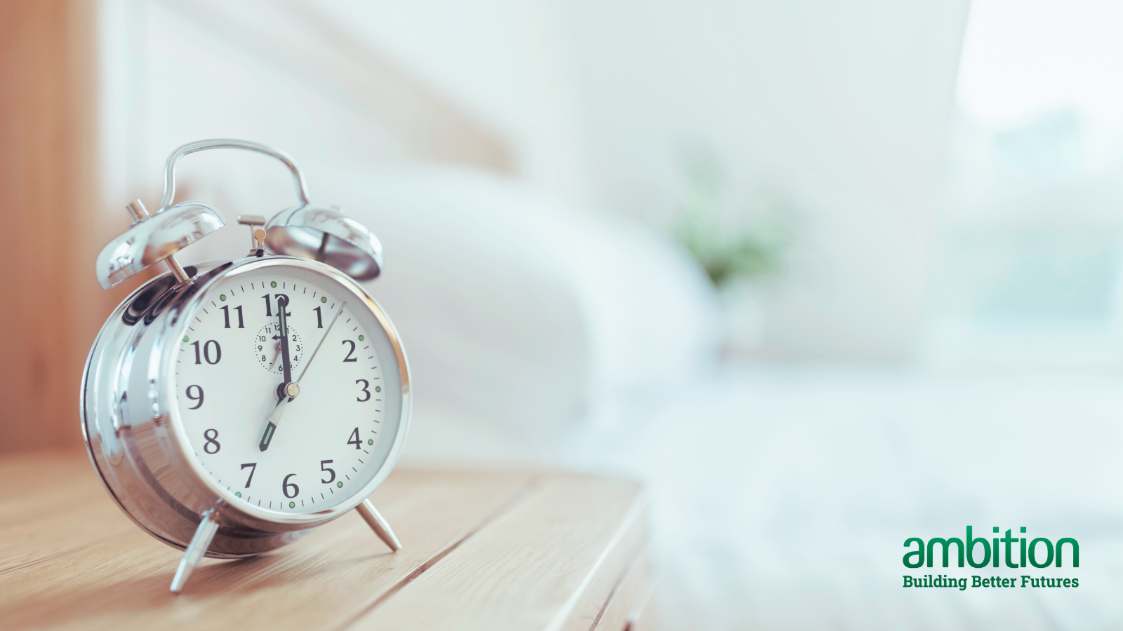 Alarm clock set to 7am, sitting on a desk next to a bed